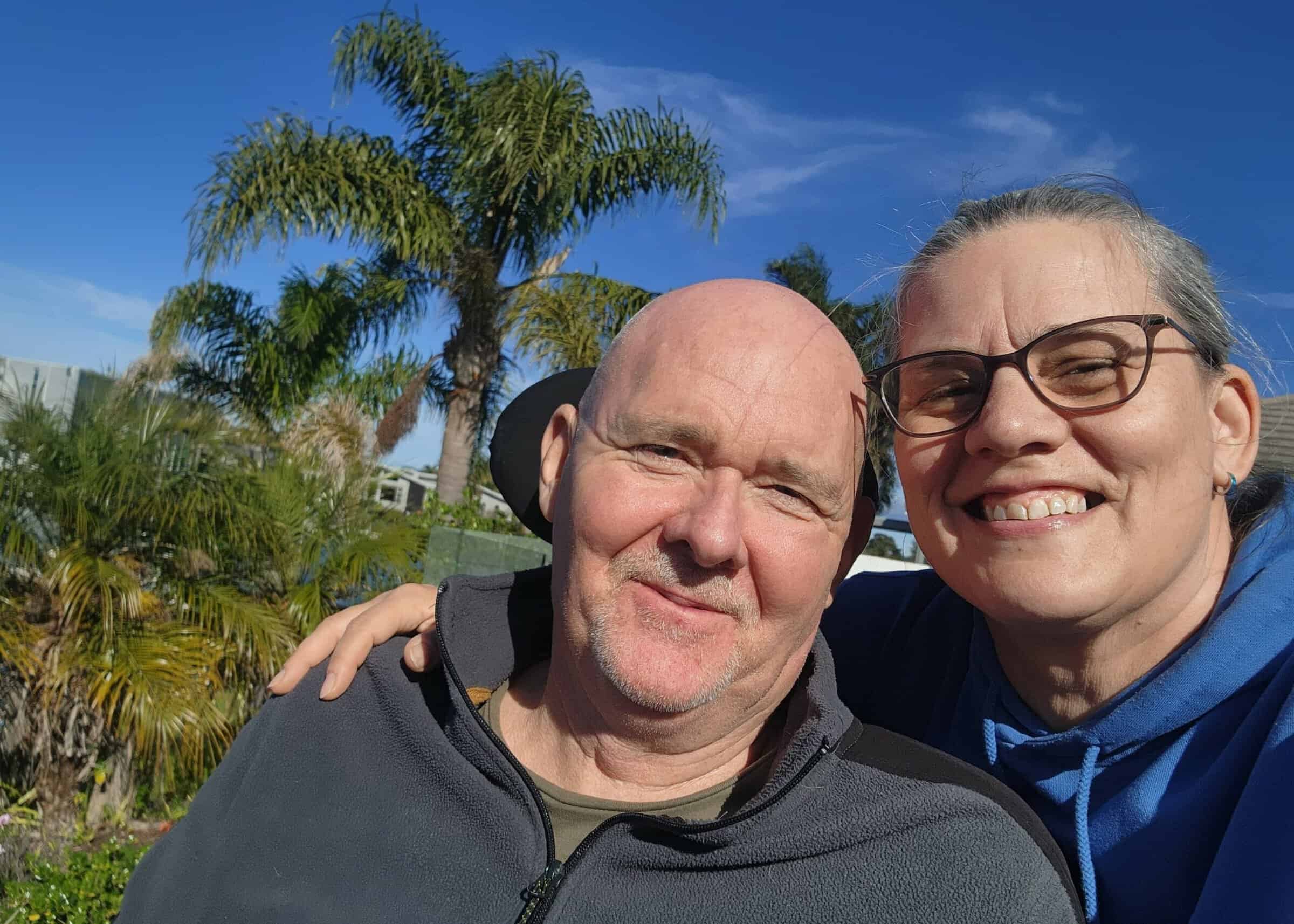 Carl And Lisa Cavanagh smile at the camera with a blue sky behind them