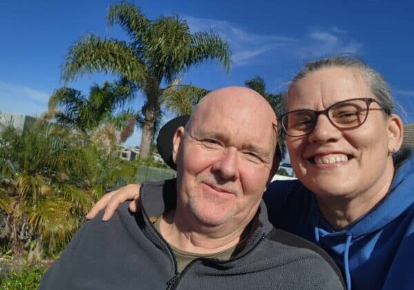 Carl And Lisa Cavanagh smile at the camera with a blue sky behind them