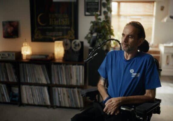 Chris Kemp sits in his living room in a power chair